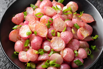 Roasted radish with spring onion and herbs in a black bowl