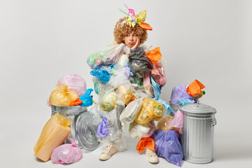 Sad eco friendly woman looks sadly away poses around garbage bins with plastic wastes around thinks...