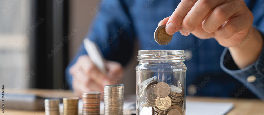 Wall mural Tax and savings finance concept, businessmen saving money concept. hand holding coins and putting them in jug glass.