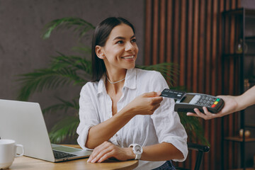 Young happy woman in white shirt hold pay waiter hold wireless bank payment terminal process...