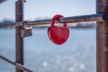A heart-shaped door lock, a symbol of love and fidelity with a lake in the background, hangs on the...