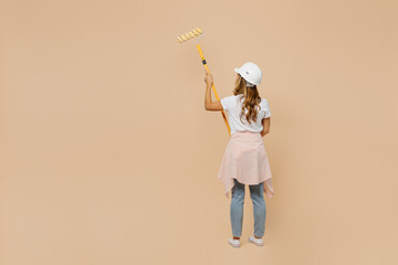 Back view full body young employee laborer handyman woman in white t-shirt helmet use roller paint walls isolated on plain beige background Instruments accessories for renovation room Repair concept.