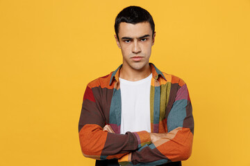 Young sad frowning unhappy middle eastern man 20s he wear casual shirt white t-shirt hold hands crossed folded look camera isolated on plain yellow background studio portrait People lifestyle concept.