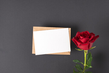 Fototapeta premium A red rose and a mock-up of a kraft envelope with a blank sheet on a black background. Banner for Valentine's Day. Postcard for February 14. Love. Minimalism.