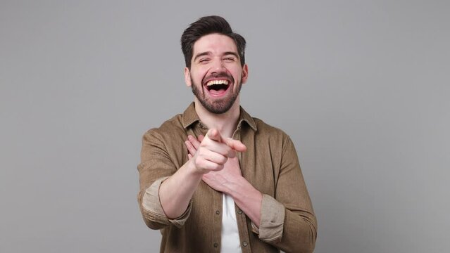 Young excited cheerful fun man 20s wear brown shirt look camera laugh smiling watch comedy movie pointing index finger on you isolated on plain grey background studio portrait People lifestyle concept