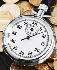 Analog stopwatch and pile of gold coins on a black background close-up. Counting time by stopwatch....