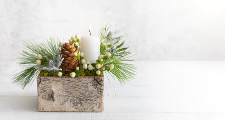 Christmas composition of candle, pine cones, fir branches, flowers and winter berries in wooden box. Cozy home winter concept.