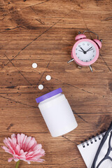 women health concept. medicine, health care style. copy space. white plastic bottle with pills, flowers, notebook and clock on wood background. 