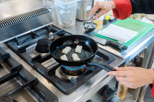 A female chef pan-frying lard pieces in restaurant kitchen