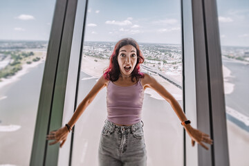 A girl with a phobia and fear of heights screams and reacts emotionally on the observation deck of the TV tower. Psychological challenge - obrazy, fototapety, plakaty