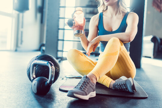 Beautiful young woman on gym floor drinking water while pausing from exercise