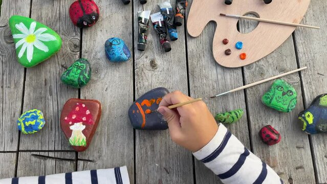 child's hands drawing a ladybug on a stone with acrylic paints. Home hobbies are authentic. Artwork on stones.