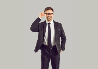 Portrait of confident young businessman in suit and glasses isolated on grey studio background. Smiling successful man CEO or boss in formalwear show leadership. Employment concept.