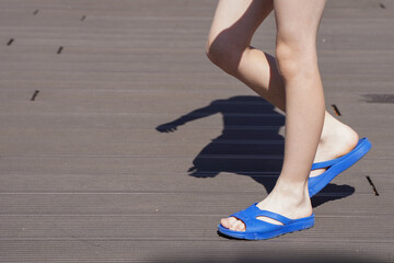 Legs of a vacationer at the resort in blue flip-flops walking on the deck near the pool