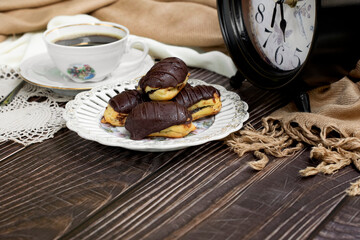 cup of coffee with eclair and vintage clock on wooden background.  coffee time concept.