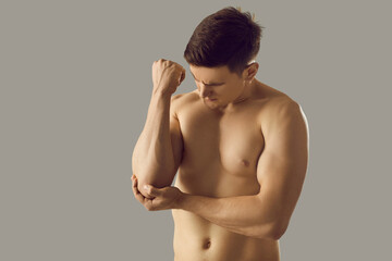 Young toned naked man on grey studio background have ache in arm. Pain in elbow cap. Fit sexy...
