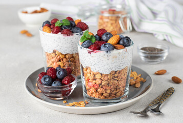 Chia seeds pudding with muesli, fresh berries and almonds in two glasses on gray plate. Healthy breakfast concept