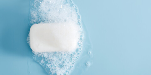 White soap bar and foam on pastel blue background. Bar of soap with bubbles. Flat lay, top view, copy space
