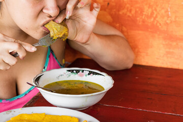 detail shot of a colombian peasant girl, having a breakfast of beef broth with yellow arepa. woman...
