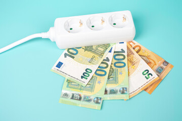 Electric power strip extension cord with Euro money banknotes on light blue background. Increasing...
