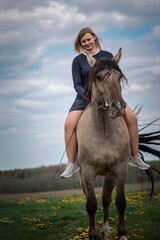 Obraz premium A young beautiful blonde girl trains a horse in the field.