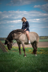 A young beautiful blonde girl trains a horse in the field.