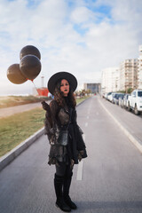 Fototapeta premium young latin woman dressed as a witch standing in the street with balloons portrait
