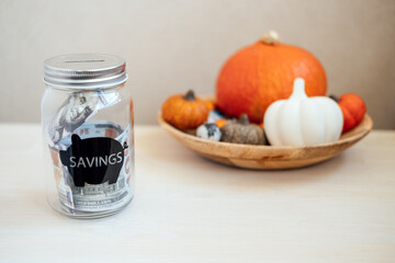 Save Money Thanksgiving day ideas, Savings, Thanksgiving on Budget. Glass mason jar piggy bank with dollars cash on Thanksgiving pumpkin decoration background