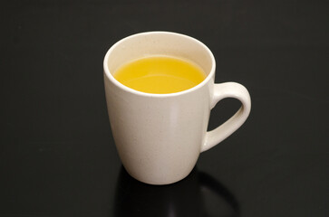 Fresh hot sea buckthorn or ginger tea in a white mug, on a black background