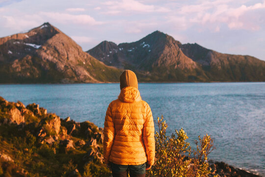 Woman traveling in Norway alone autumn season adventure lifestyle outdoor sunset mountains and fjord view winter down jacket clothing