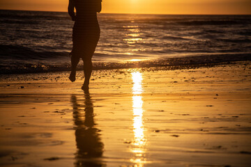 Woman in dress running towards the sea at sunset