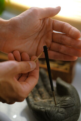 A match in the palms ignites an incense stick