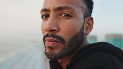 Close-up, young bearded male athlete standing on the embankment, looking at the sea. Guy turns his head and looks at the camera.