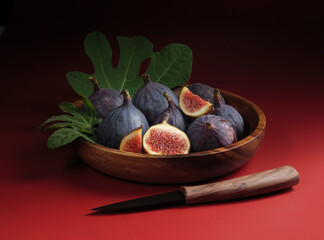 Still still with fig fruits in a wooden plate with green leaves and a knife. Sweet dessert for a vegan menu with fresh figs on red background.