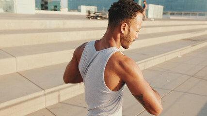 Close up, young bearded male athlete doing workout, stretching on the embankment