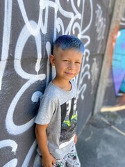  cute funny boy with bright blue colored hair on a background of a colored wall with graffiti