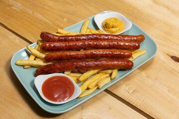Grilled sausages served with french fries with dips on a plate