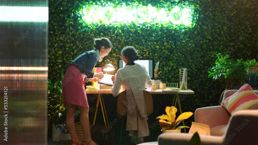 Poster Manager consulting an employee on a digital tablet while working on a web design with laptop. Woman employee planning website development strategy on computer while discussing project with colleague.