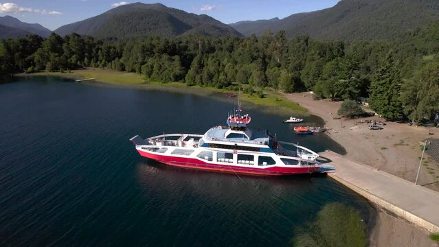 vista desde dron rodeando una barcaza barco tipo ferry para pasajeros y turistas esperando en un lago. Se ven las monta&ntilde;as y bosque de fondo..