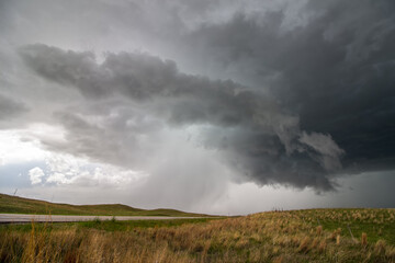 Fototapeta na wymiar A supercell thunderstorm rains and hails over a highway in hilly grassland landscape.