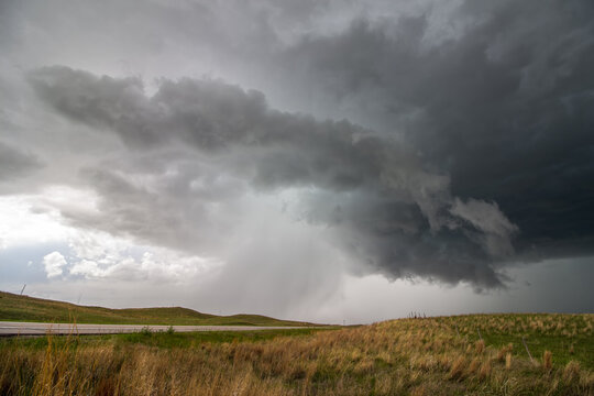 A supercell thunderstorm rains and hails over a highway in hilly grassland landscape. © Dan Ross