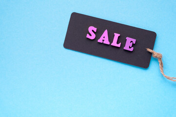 Sale - made from wooden color letters on black paper price tags on string. Labels on light blue background. Copy space, top view.