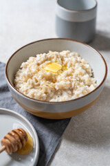 Unusual healthy delicious rice pudding made from brown rice and plant based milk served with butter and honey in grey bowl