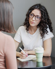 Spanish woman psychologist or business coach conducts a session with a client and takes notes in a...