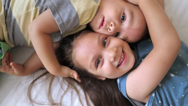 Top view portrait of happy laughing two children, sister and brother, lying head to head on the mattress in new bedroom and having fun, looking at camera. Children friendship,happy careless childhood