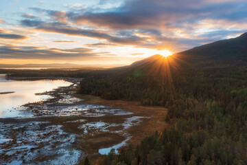 The sun rises over the mountains, forest and sea. Sunbeams shine on the morning dawn in the north