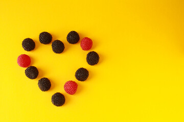 Candy heart. Blackberry raspberry jelly gummy candy sweets on yellow color background. Space for...