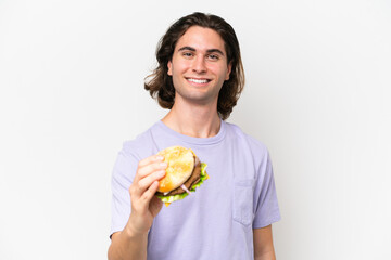 Young handsome man holding a burger isolated on white background with happy expression