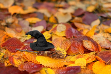 broom and witch hat on autumn leaves natural background close up. symbol of Halloween holiday,...