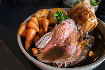 Roast beef slices on a plate with carrots, roast potatoes, a Yorkshire pudding and gravy, making a...